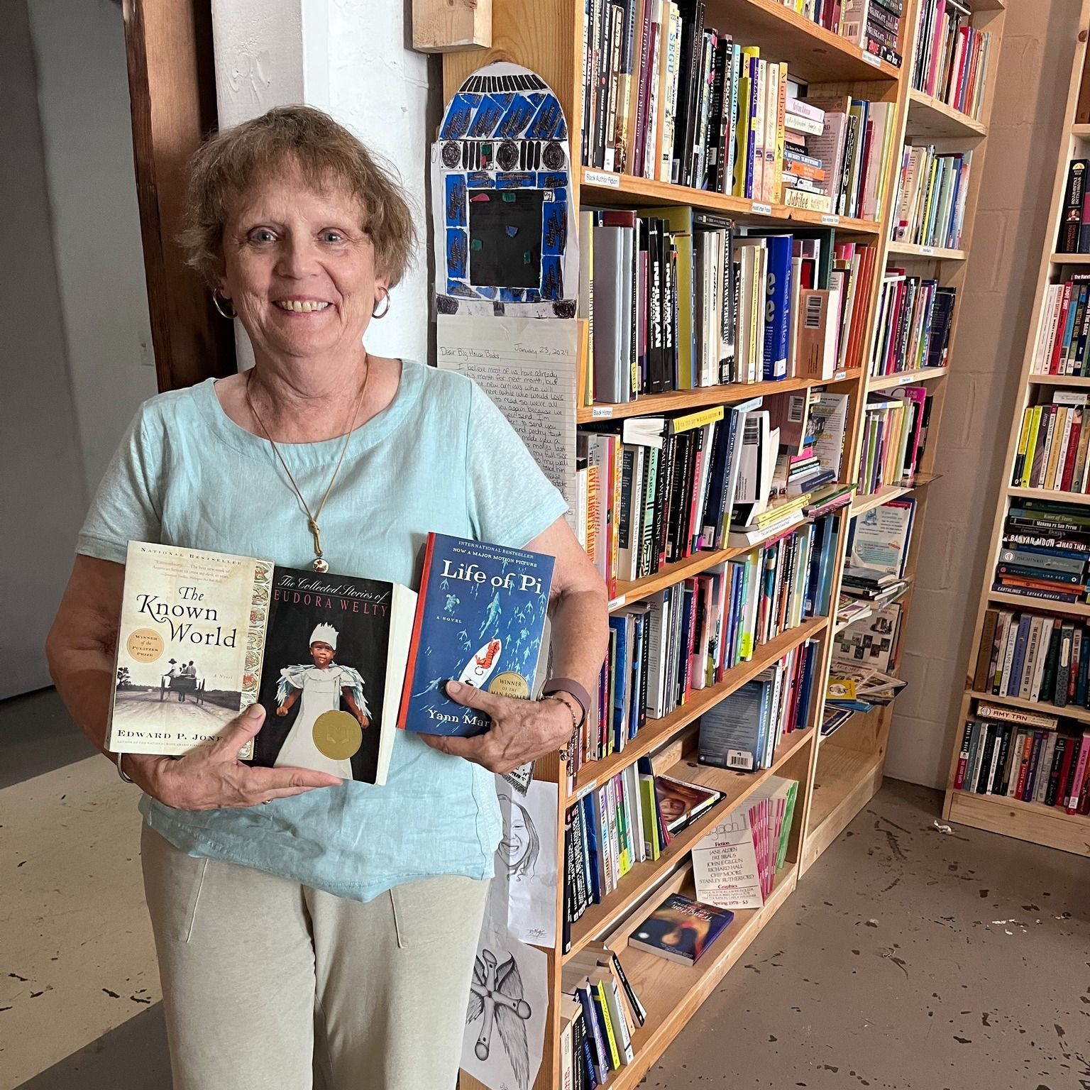 Woman smiling, holding books in a bookstore with bookshelves.