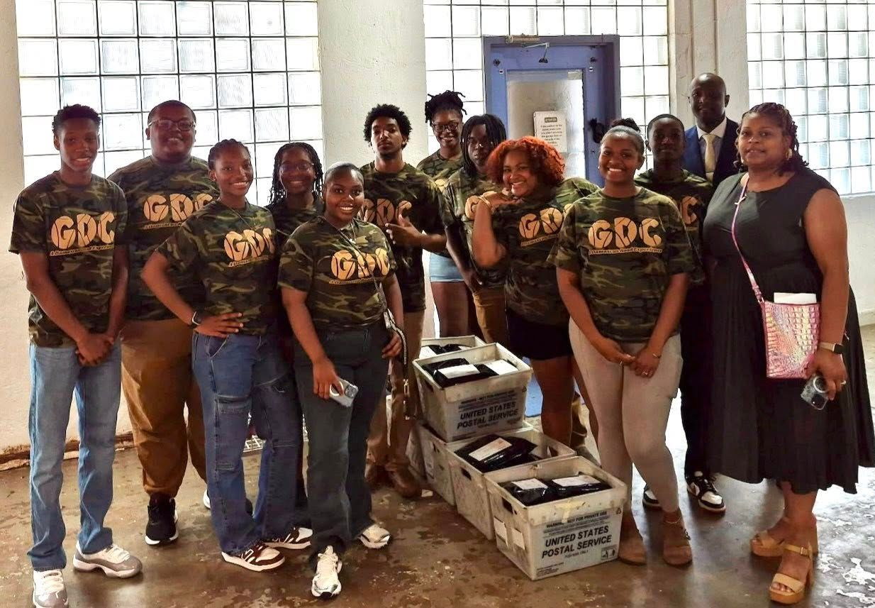 Group of people wearing camouflage shirts posing with boxes in a building. 