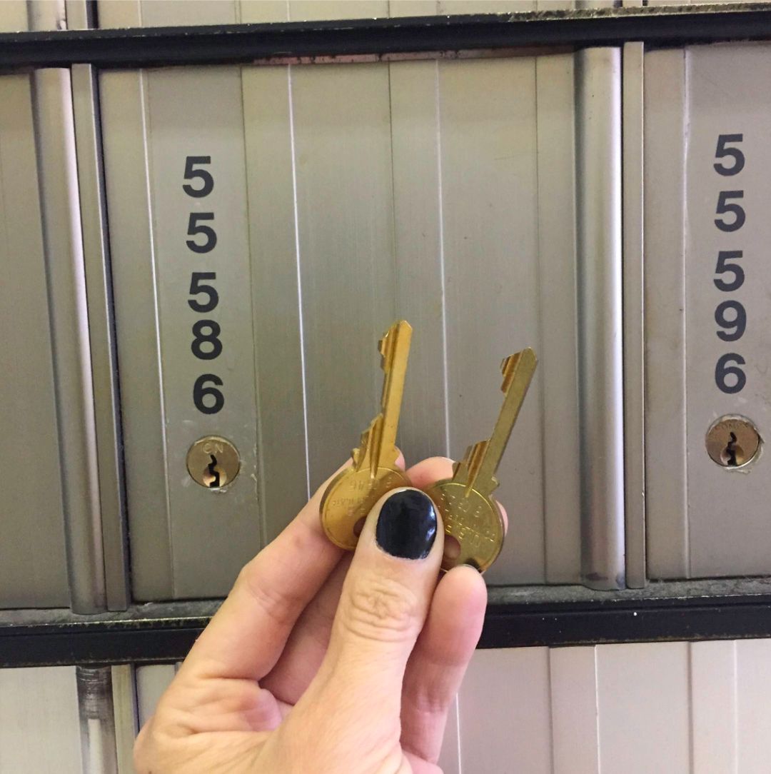 Hand holding two keys in front of a bank of mailboxes with numbers 55586 and 55596.