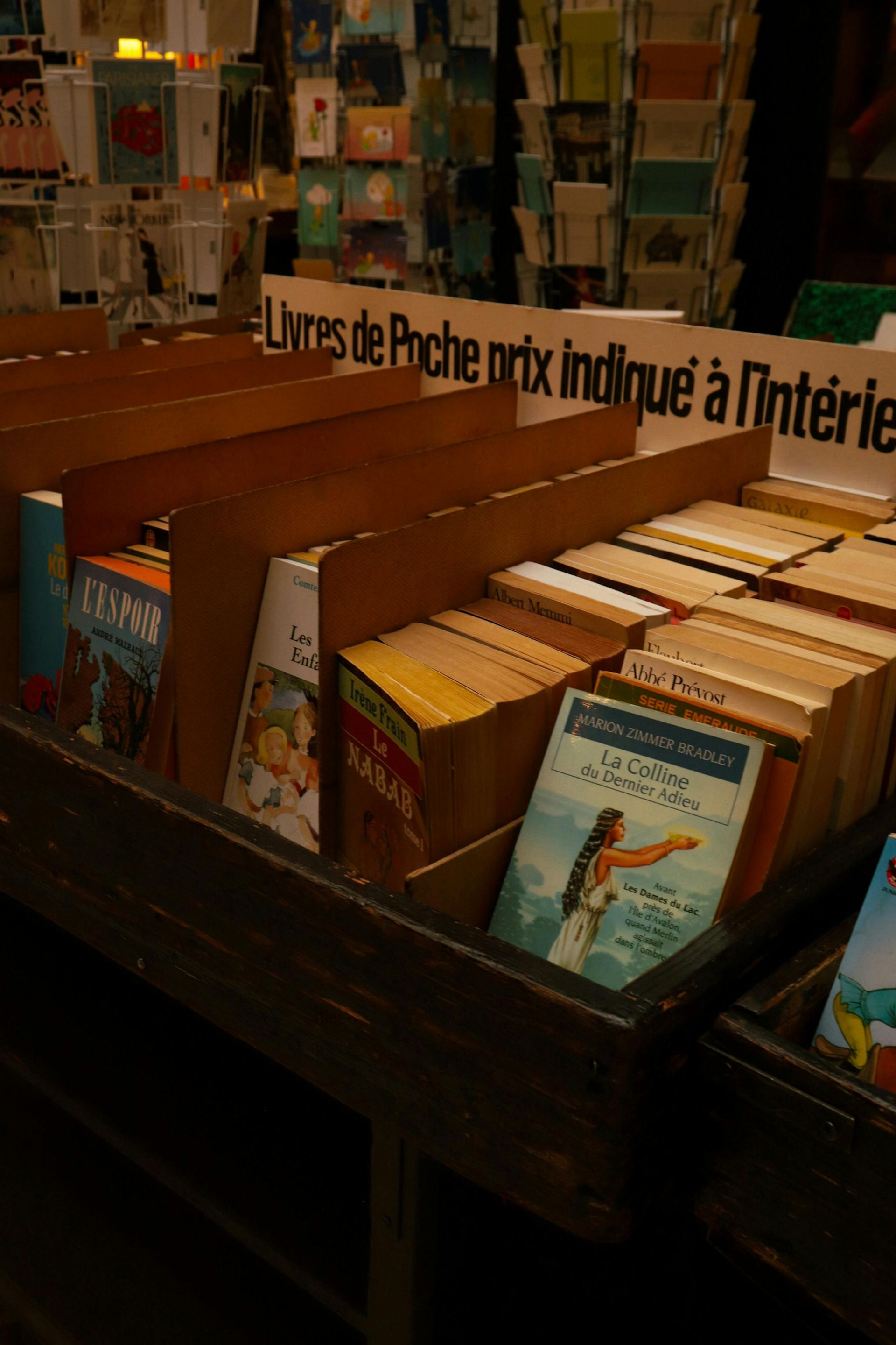 Books in a wooden bin at a bookshop, with a sign in French.