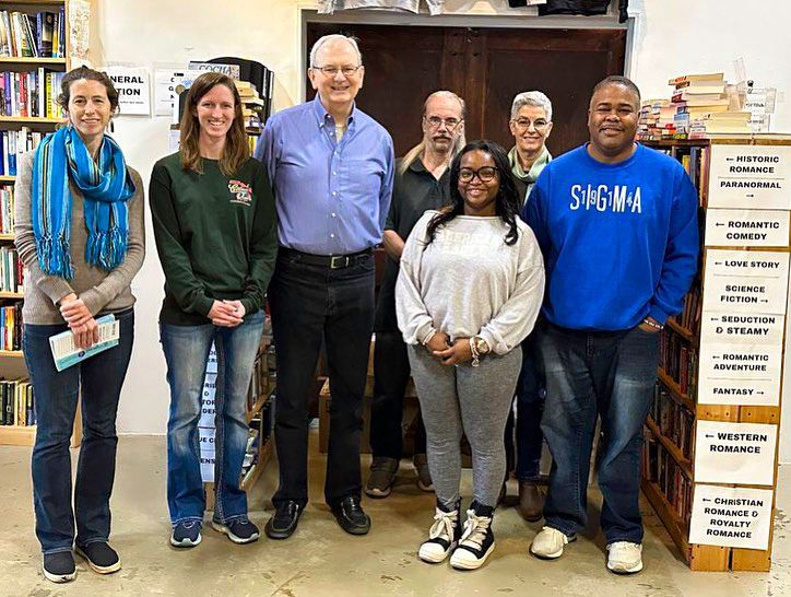 Group of people standing in a bookstore, smiling. Bookshelves are visible on the sides.