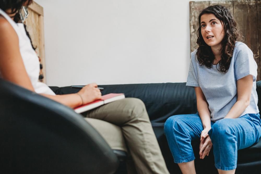 A Woman in Blue Jeans Talks to a Therapist in a Room — EastCoast Women's Centre In Caboolture, QLD