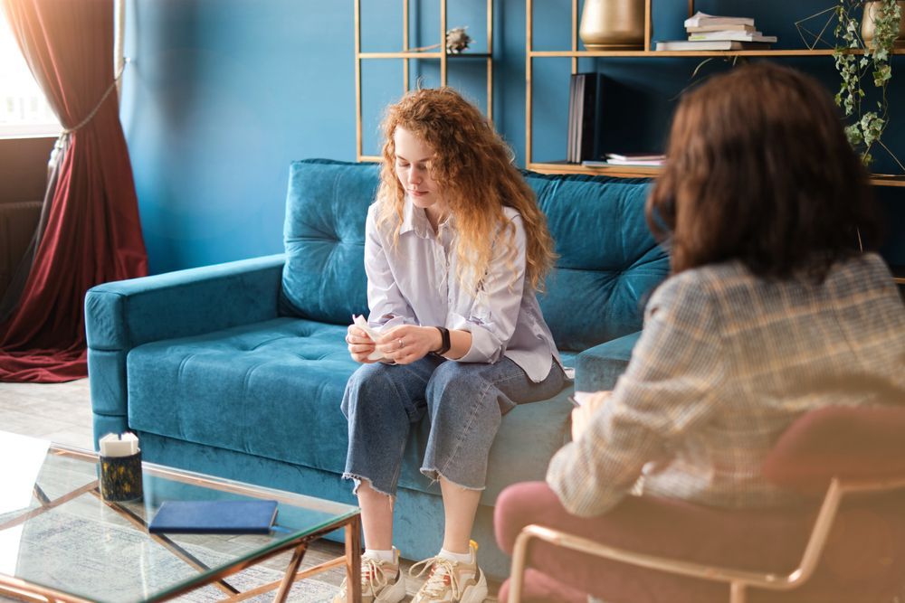 Woman With Red Hair Sitting on a Blue Couch, Looking Down, in a Therapy Session — EastCoast Women's Centre In Gladstone, QLD