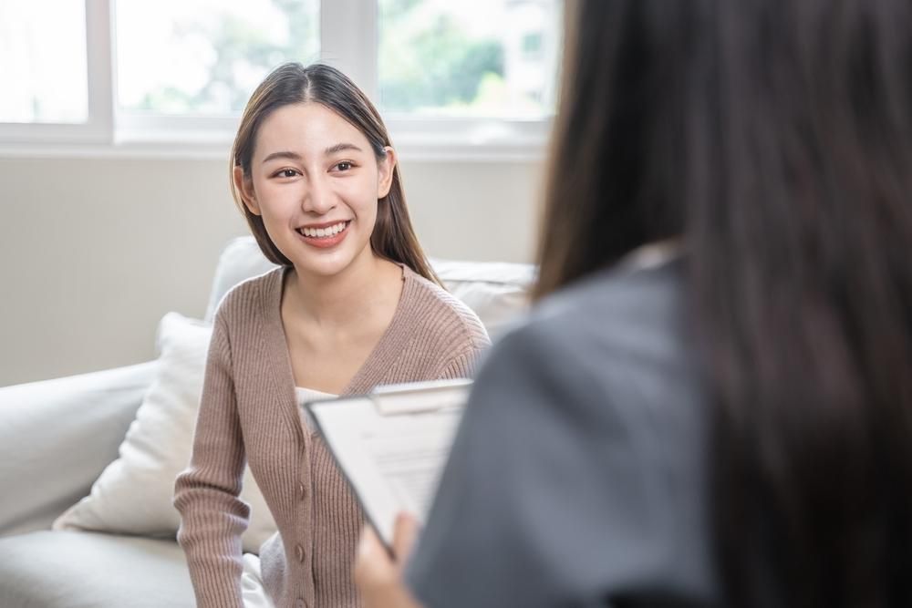 Woman Smiling While Seated on a Couch and Talking to Someone — EastCoast Women's Centre In Redcliffe, QLD