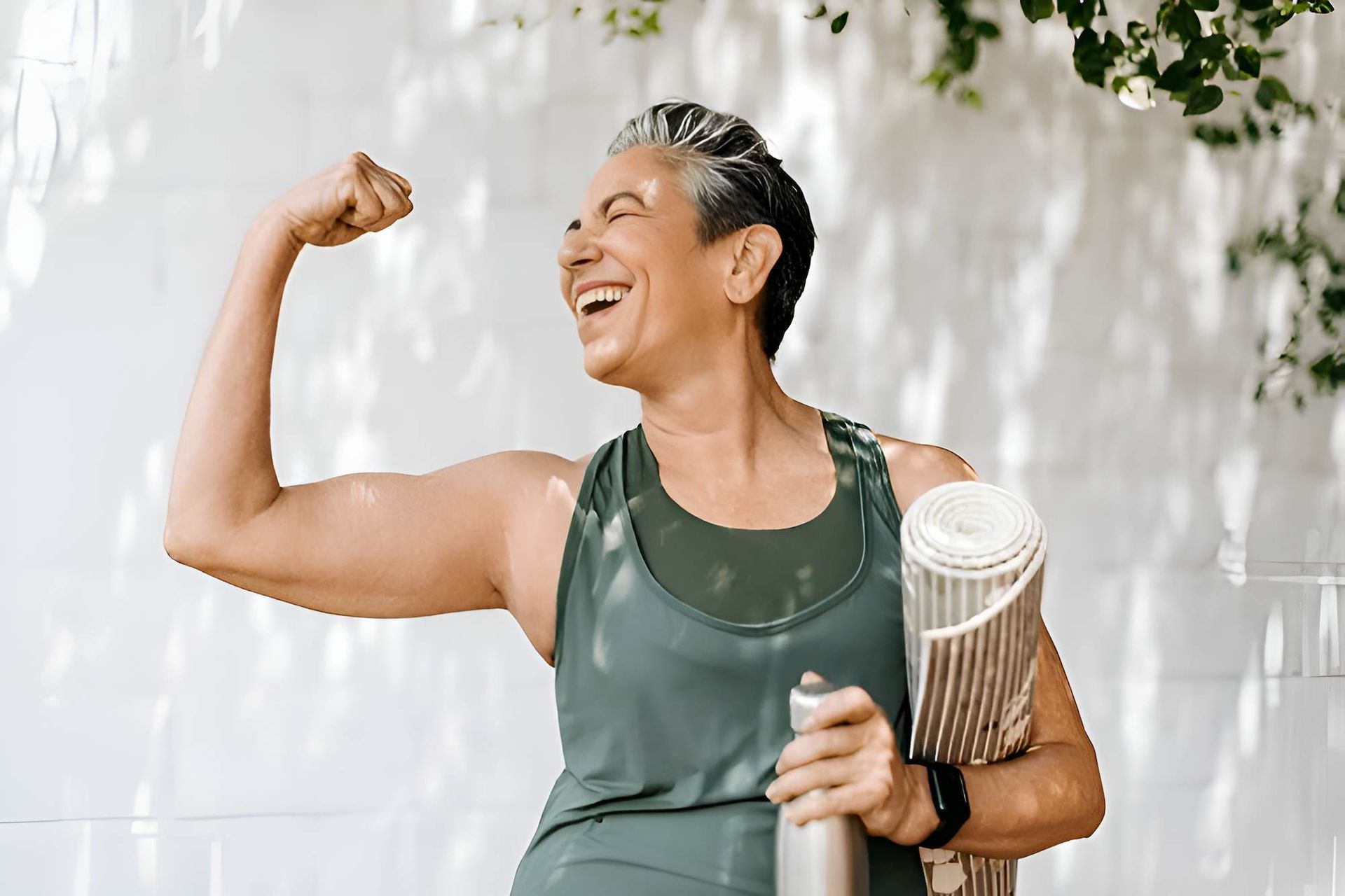 An Older Woman is Holding a Yoga Mat and Flexing Her Muscles — Eastcoast Women's Centre in Emerald, QLD