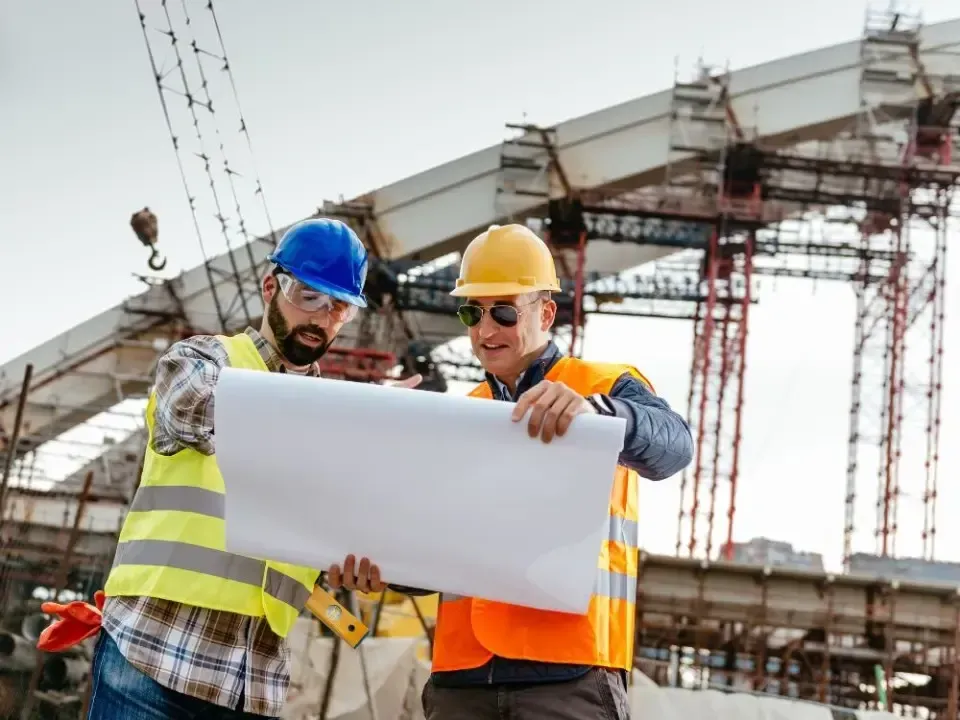 Two construction workers are looking at a blueprint at a construction site.