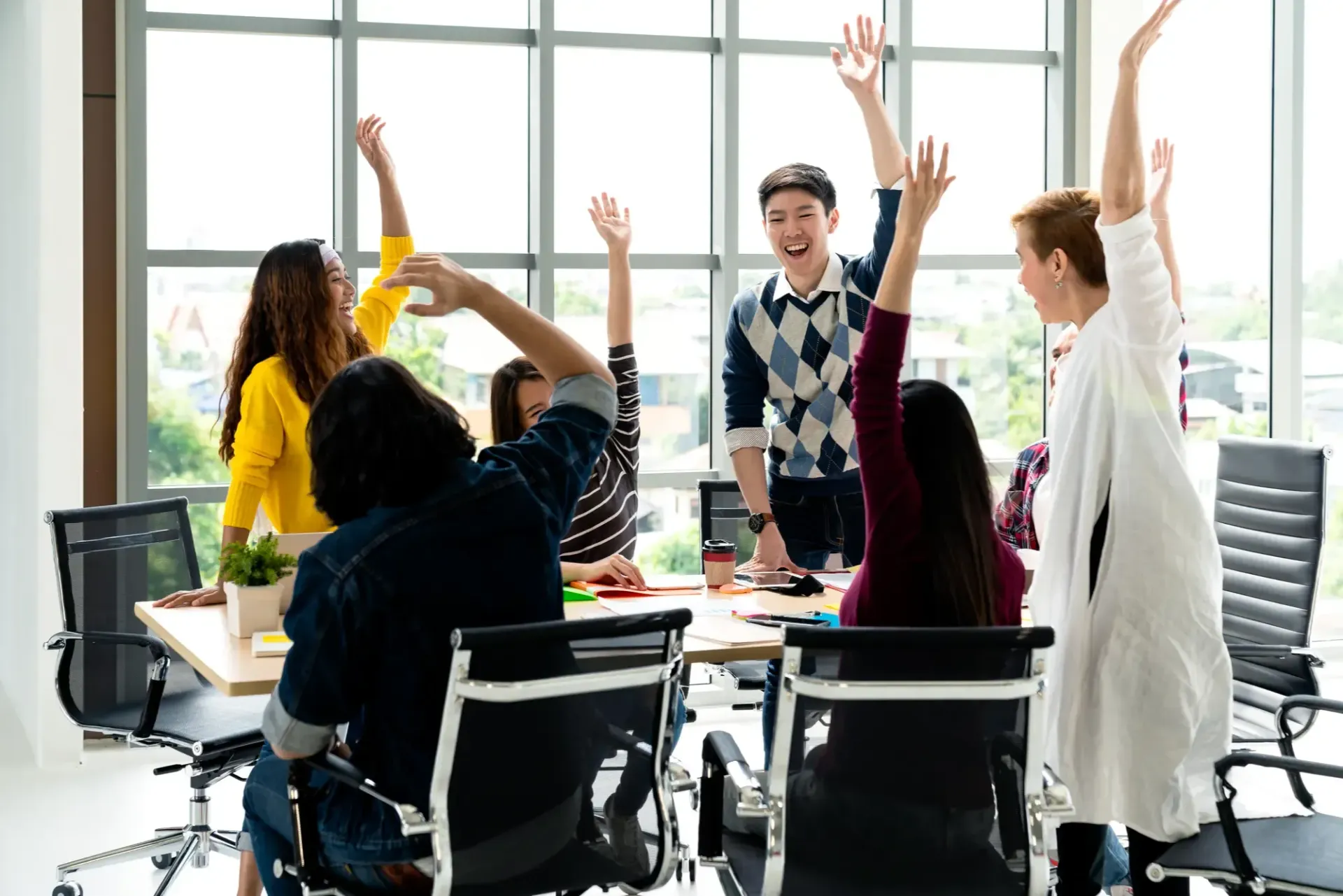 A group of employees are sitting around a table with their hands in the air.