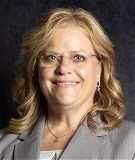 A woman in a suit and glasses is smiling for the camera.