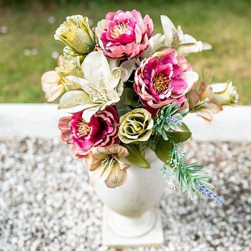 A vase filled with flowers is sitting on a gravel surface.