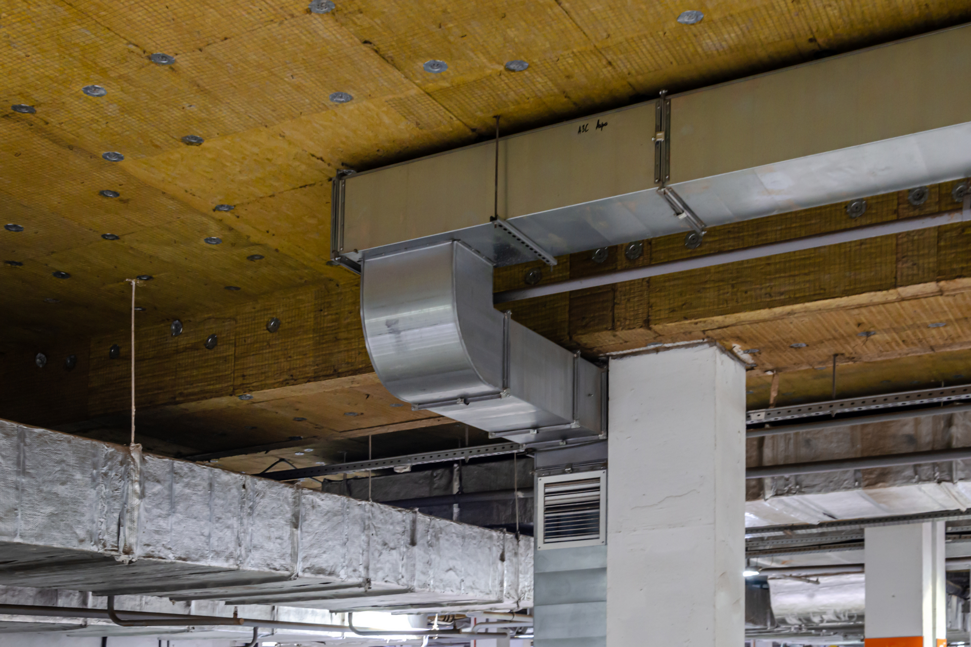 HVAC ductwork and insulation installed on a concrete ceiling with metal beams and a white support column.