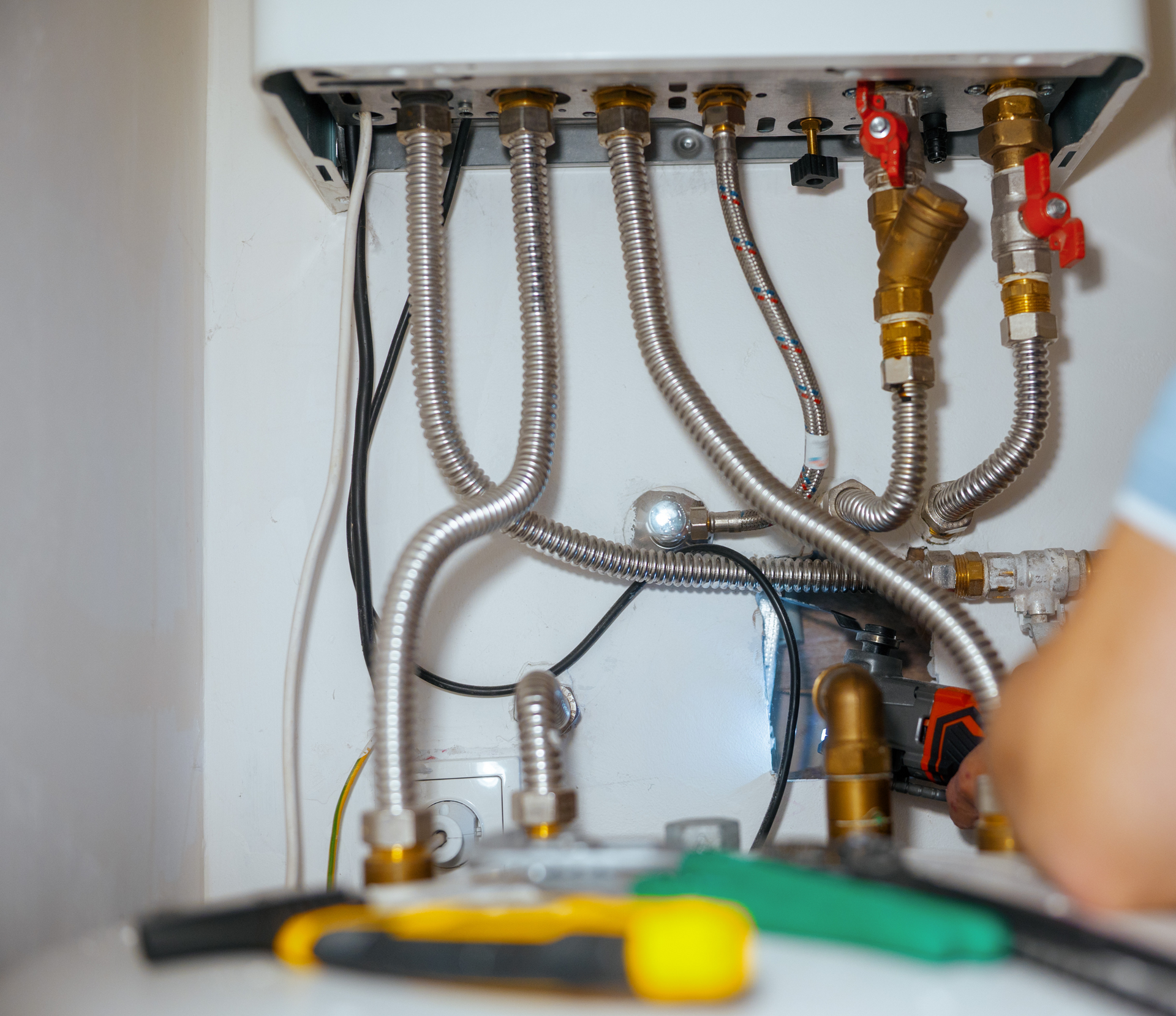 Plumber working on a boiler, visible pipes, valves, and tools.
