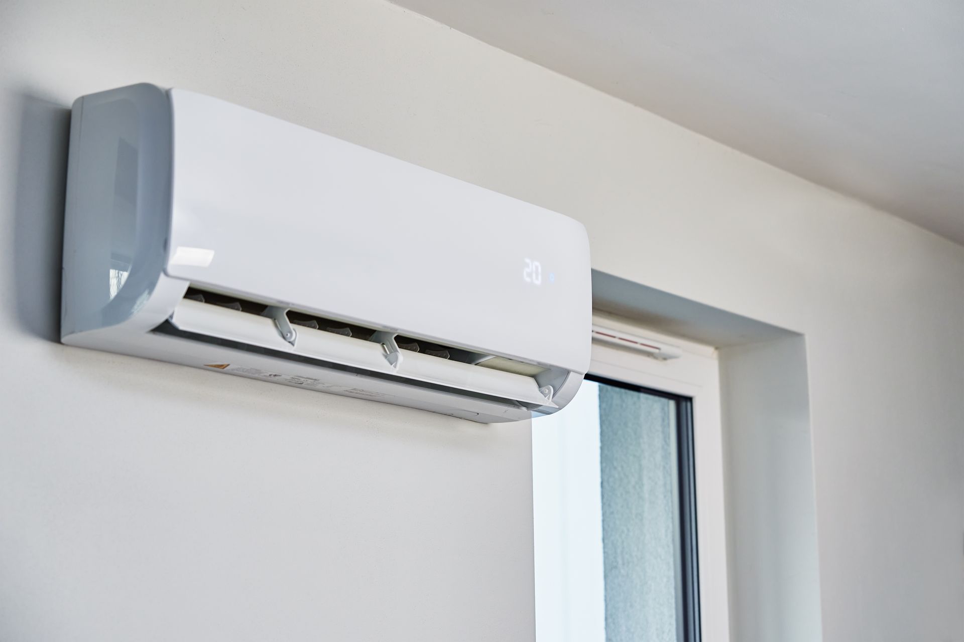 White wall-mounted ductless min split unit above a window, interior shot.