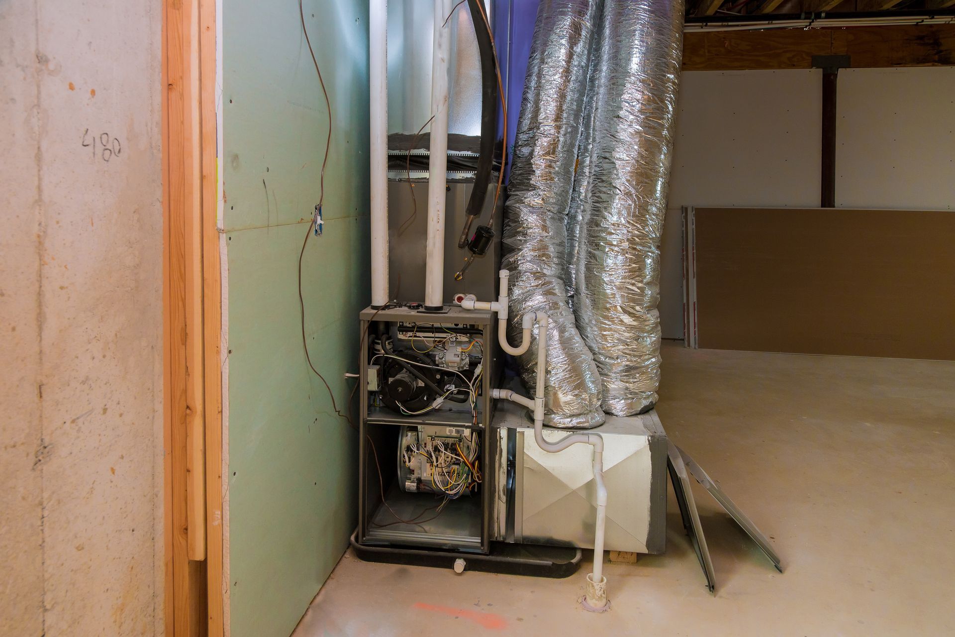 Furnace unit in a basement, with ductwork and a partially finished wall.
