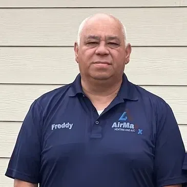 Man in blue polo shirt with company logo, standing in front of a light-colored building.