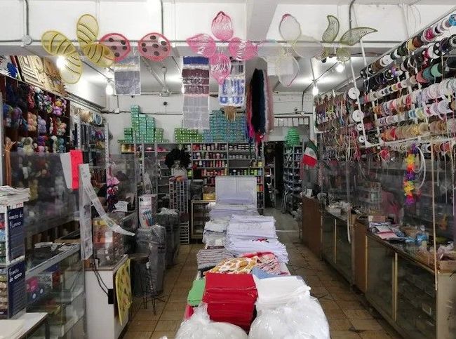 Interior de una tienda de artículos para manualidades; estantes llenos de cintas, telas y accesorios de colores.