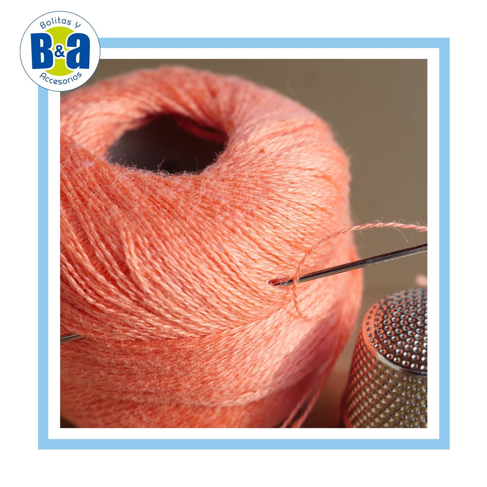 Primer plano de una madeja de hilo color melocotón con una aguja y un dedal.