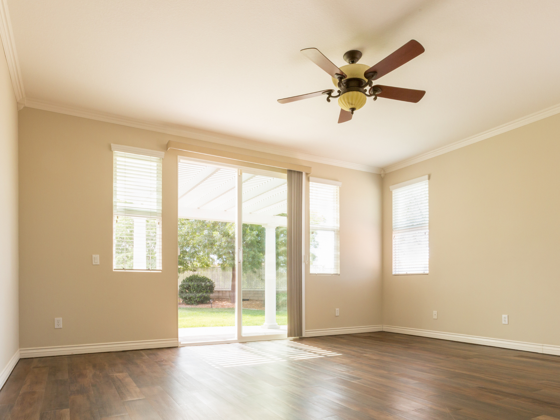 A cream-colored living room with a ceiling fan and sliding glass doors.