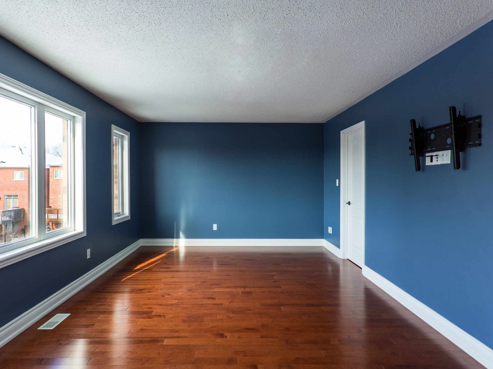 An empty living room with blue walls and hardwood floors, and white trim