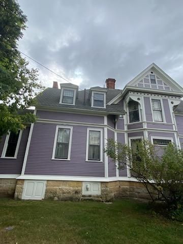 A large purple house with a gray roof is sitting on top of a lush green field.