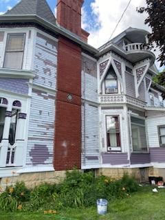 A large white and purple house with a red chimney is being painted.