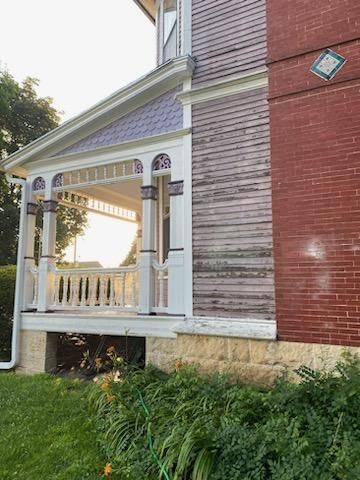 There is a porch on the side of a brick house before renovation
