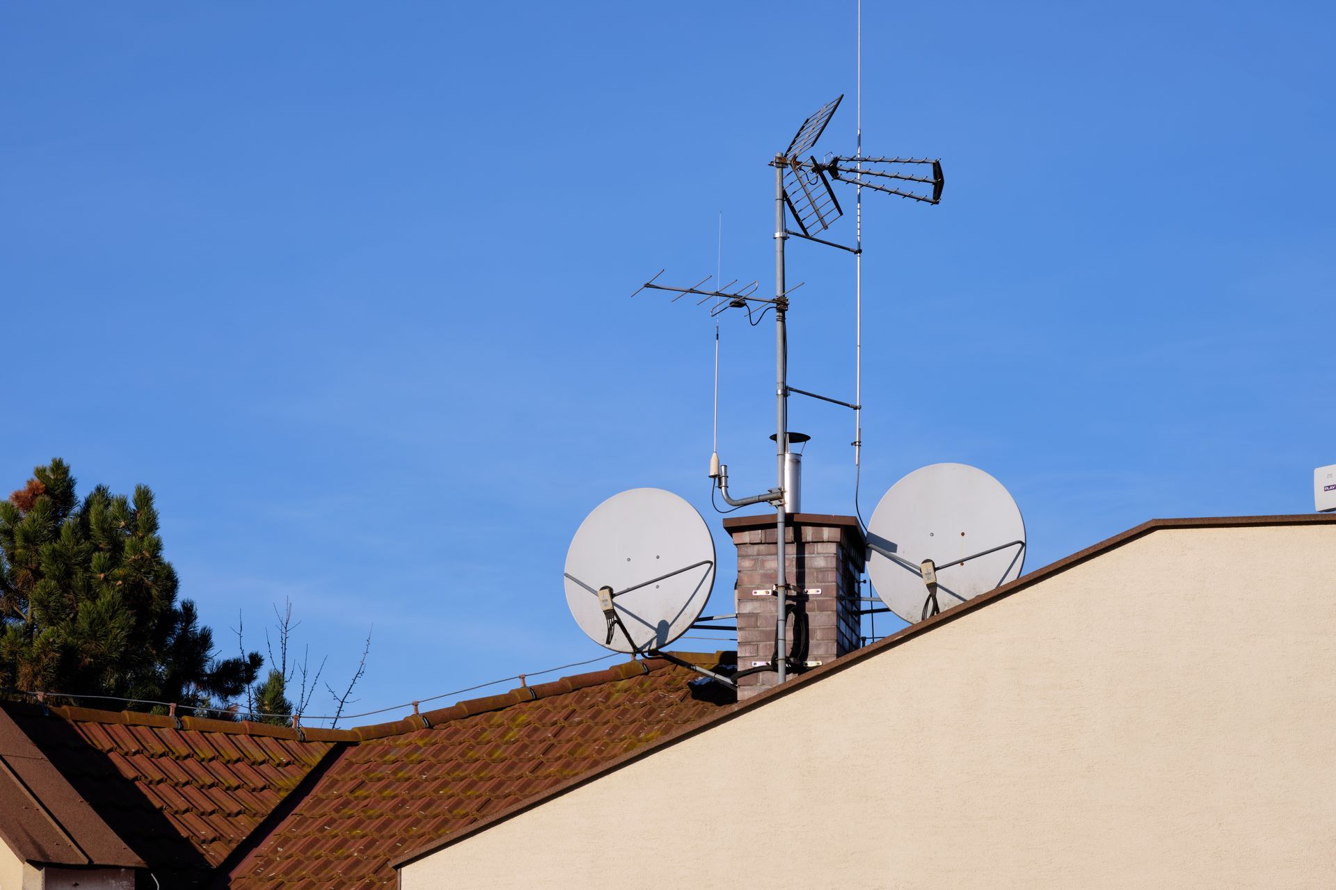 Person in blue jacket adjusting antenna on rooftop. City in background.