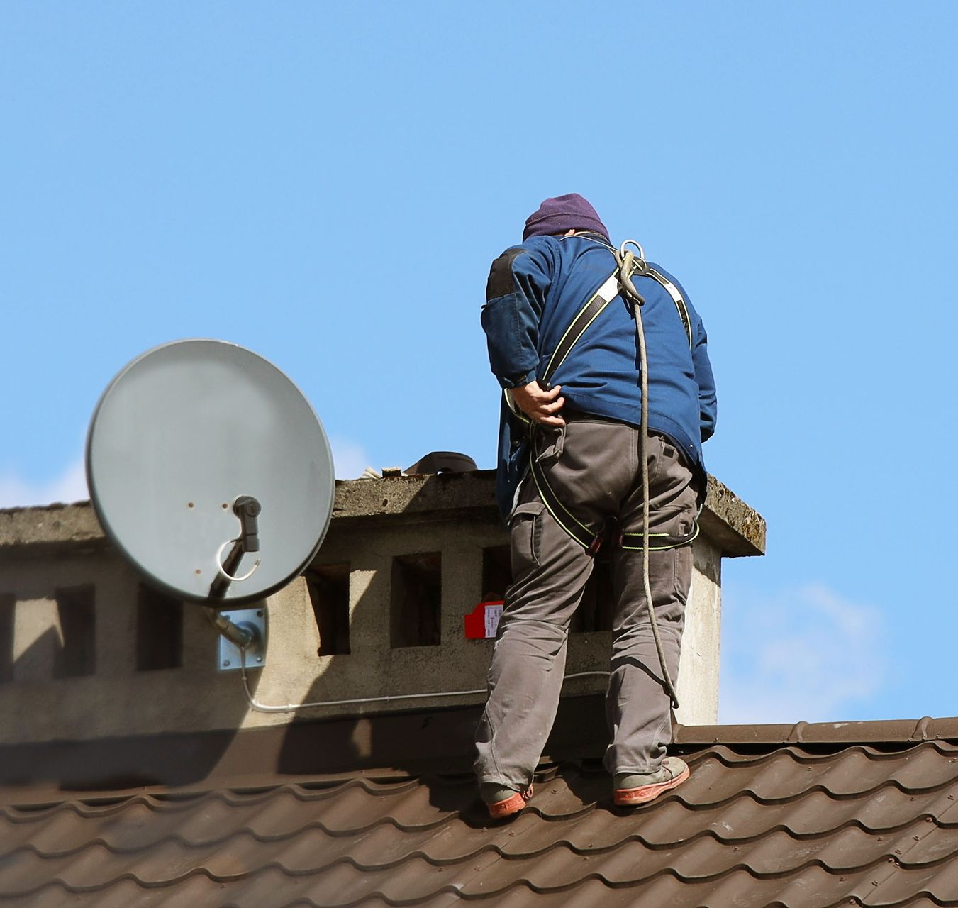 Person in blue jacket adjusting antennas on a rooftop tower, city backdrop. Person in blue jacket adjusting antennas on a rooftop tower, city backdrop.