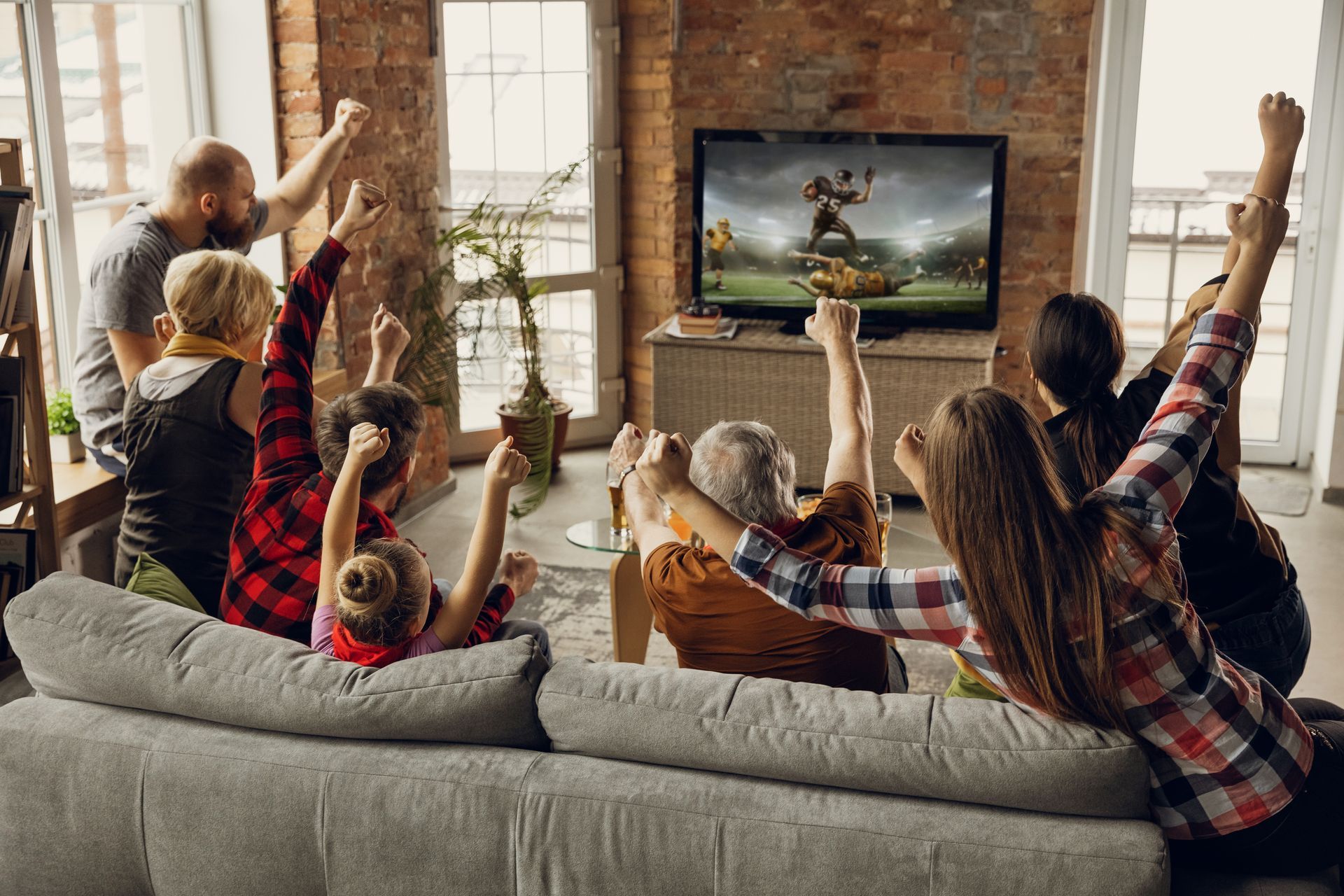 People cheering at TV, watching football in a living room; some with arms raised.