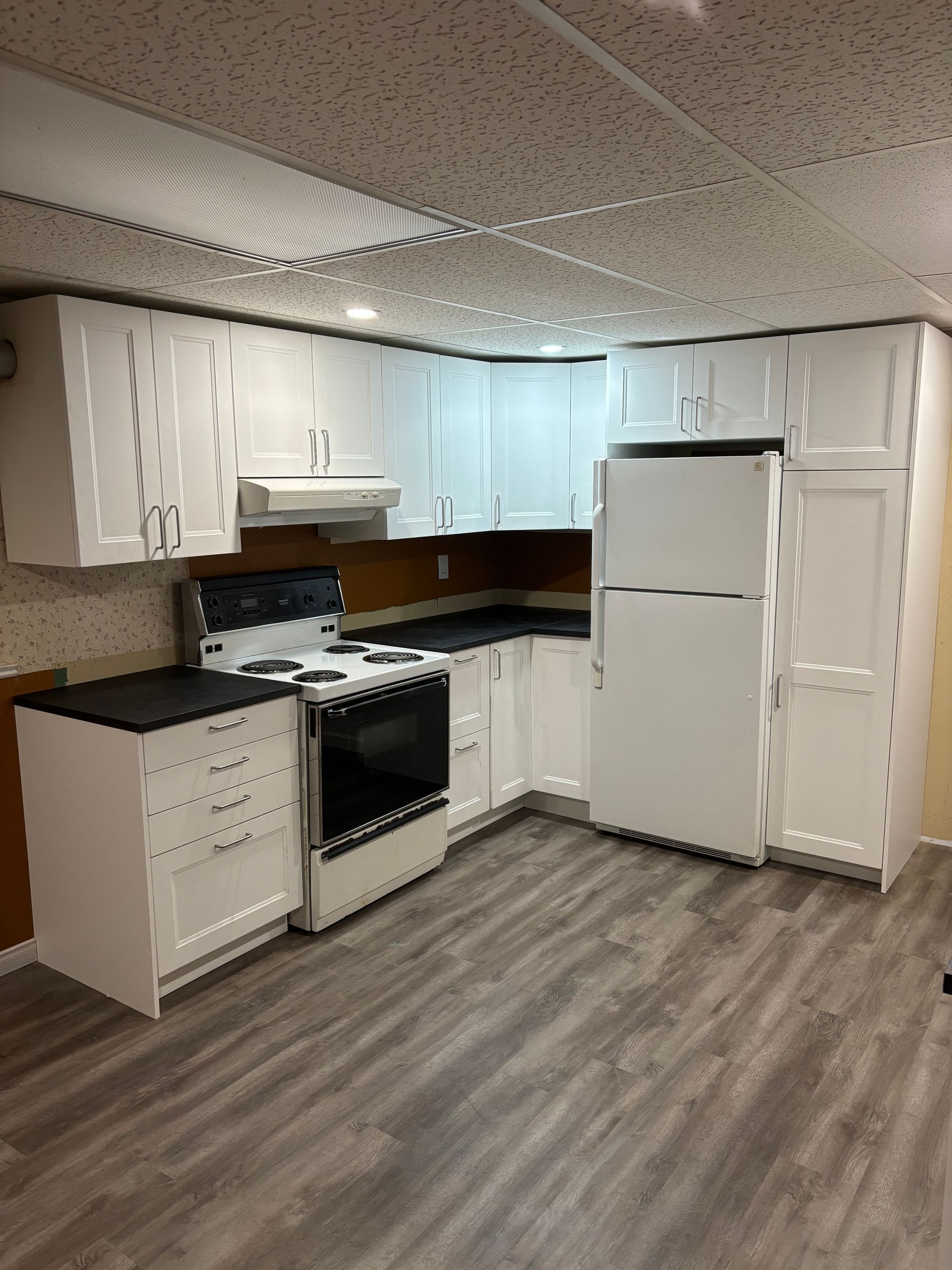 Une cuisine avec des armoires blanches, une cuisinière, un réfrigérateur et un plancher en bois.