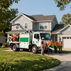 Utility workers in orange vests beside a white bucket truck in front of a suburban house