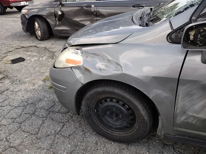 Damaged gray car with a dented front fender, parked next to a damaged black car.