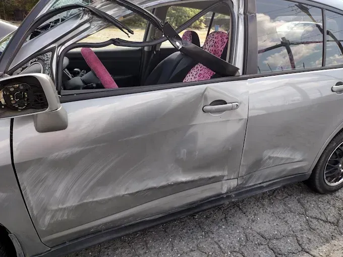 Damaged silver car with significant side damage, bent frame and broken windows.