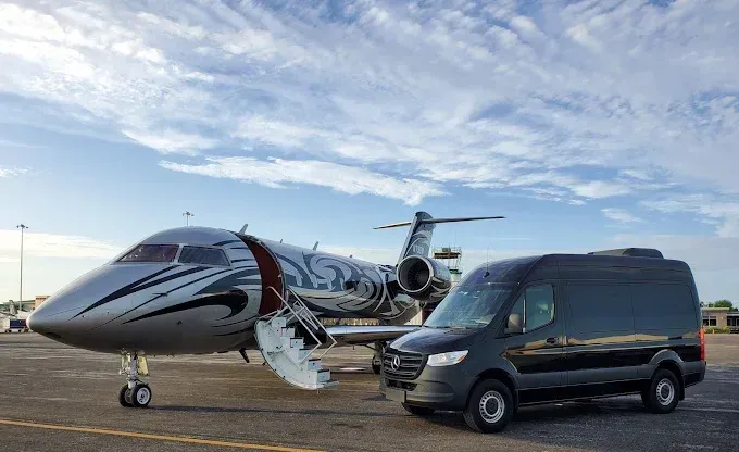 A private jet and black van parked on a tarmac under a cloudy sky.
