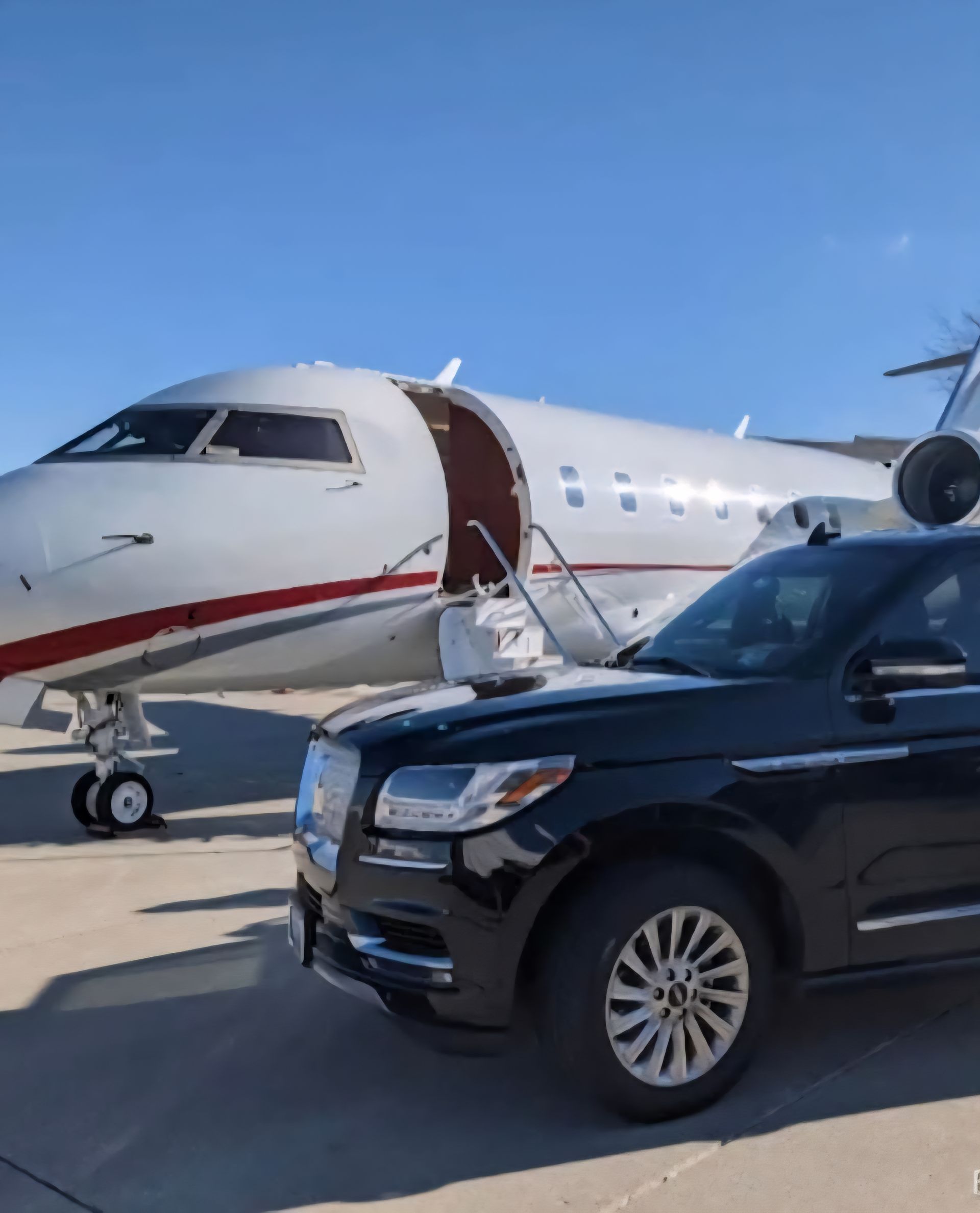 A private jet with a black van parked on the tarmac under a partly cloudy sky.