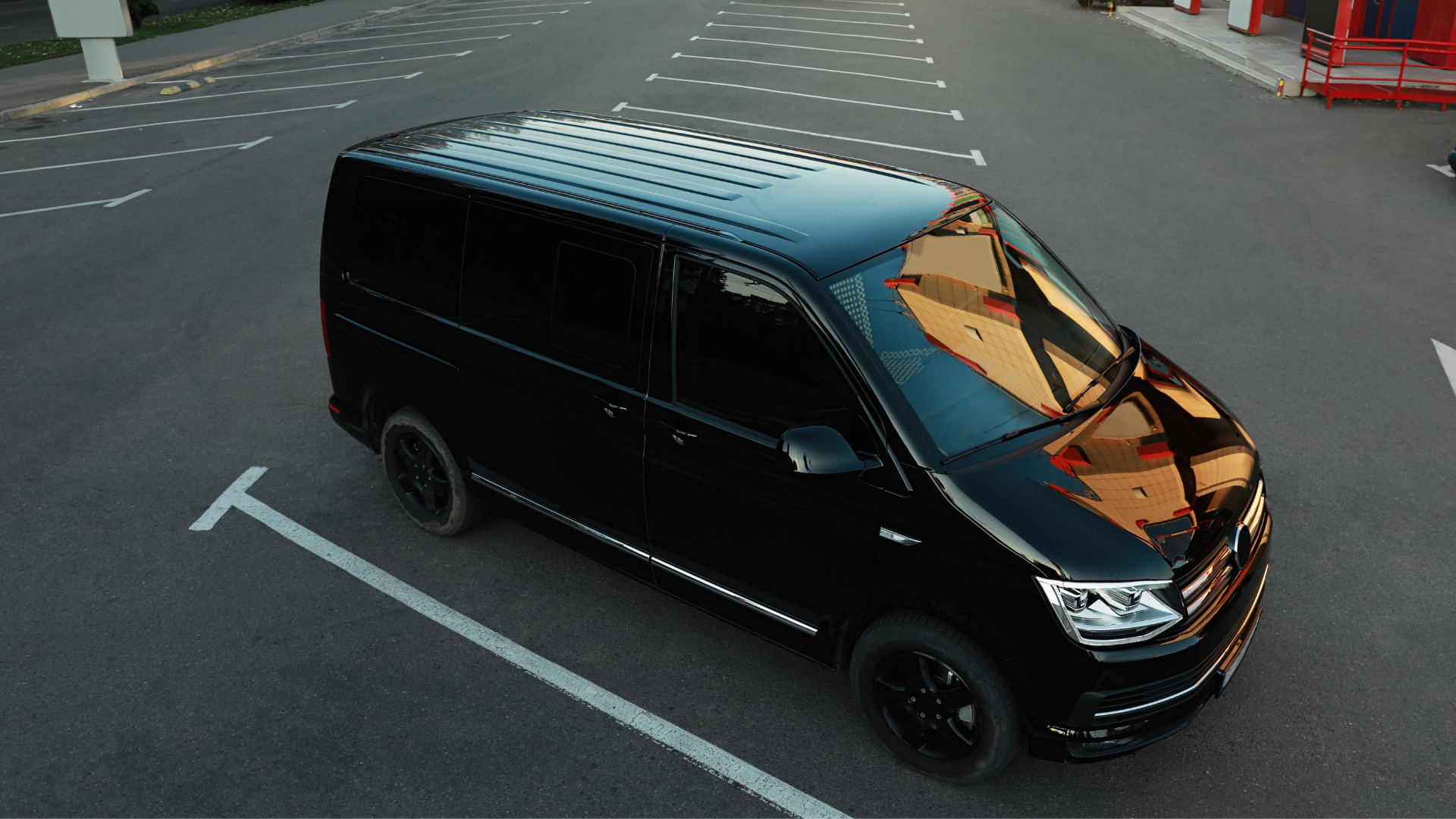 Black van parked in an asphalt parking lot. The van has black wheels and tinted windows, and the setting is outdoors.