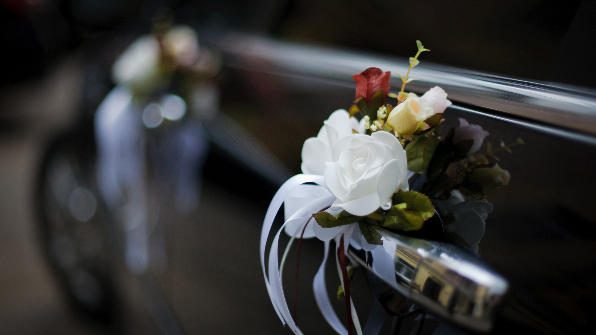 Wedding car door decorated with white and red flowers and white ribbons.