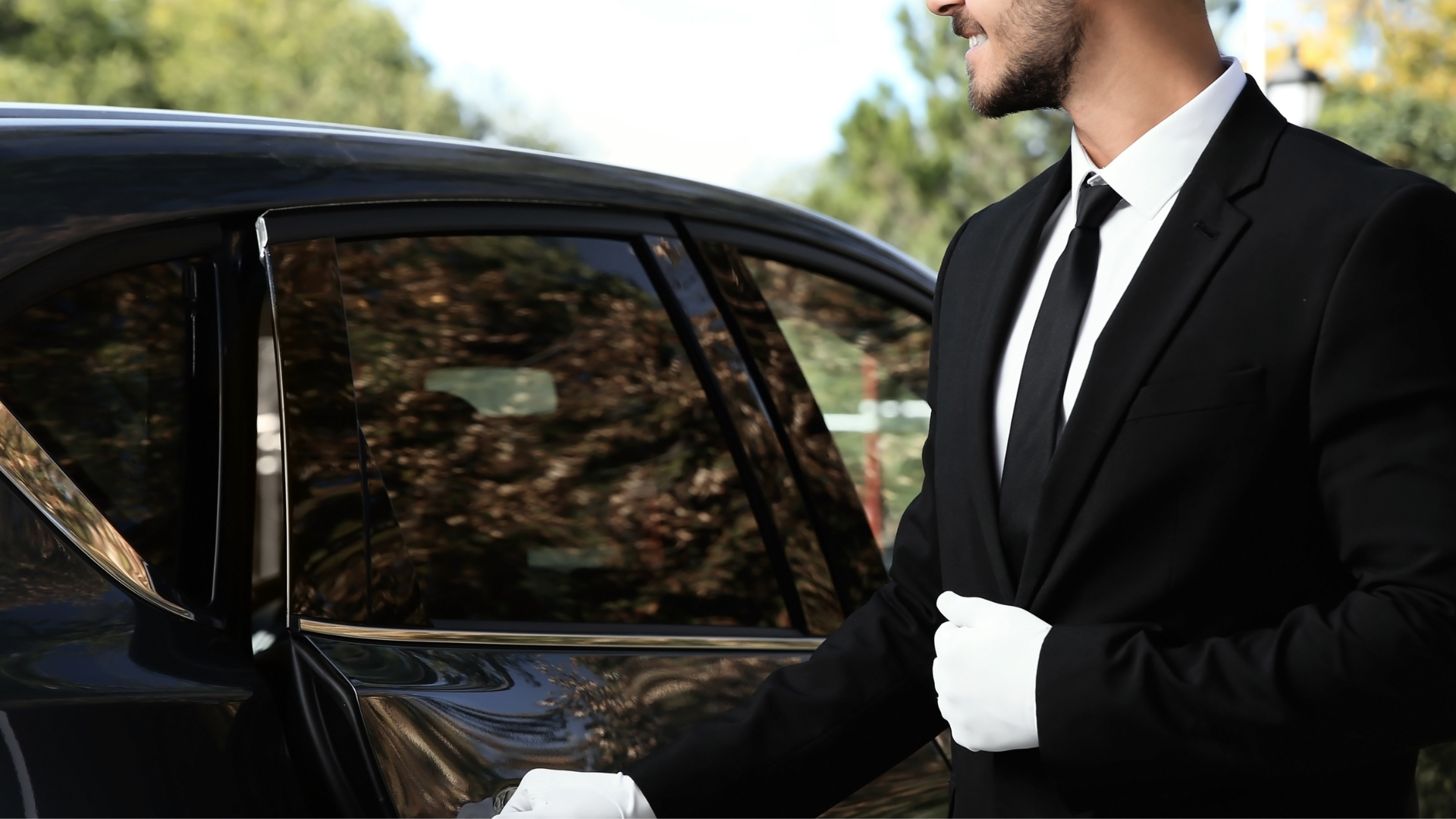 A suited chauffeur opening a black car door, ready to serve a client.