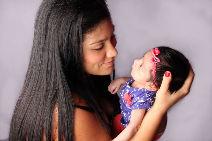 Woman holding a baby, gazing lovingly. Baby wears a headband and purple outfit.