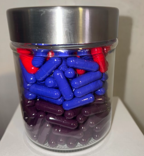 A glass jar filled with red, blue, and purple capsules, topped with a silver lid.