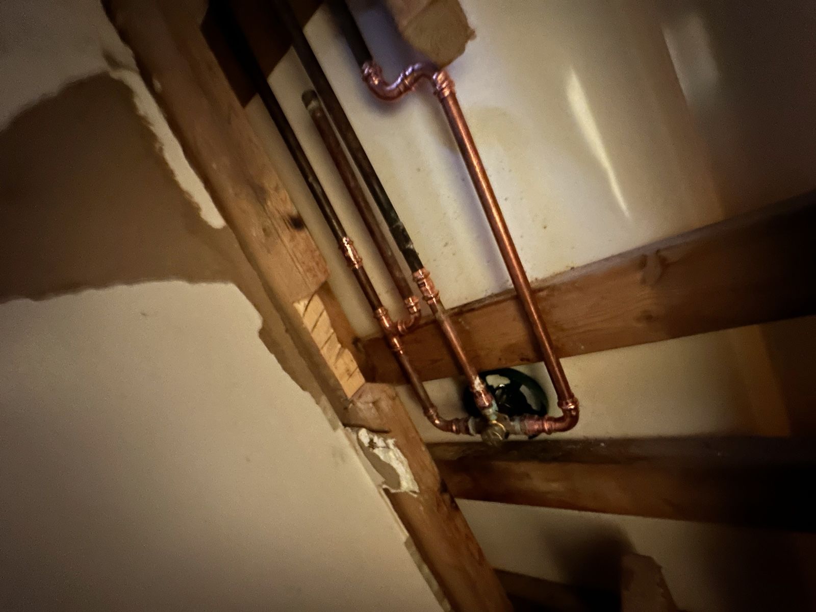 Copper pipes attached to wood beams in a wall cavity, with a black valve.