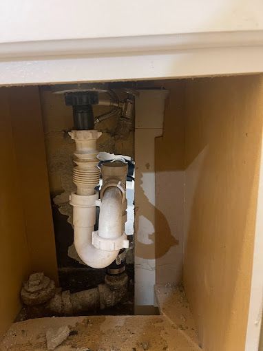 A plumbing system under a sink, featuring white pipes and a curved trap, viewed from inside the cabinet.