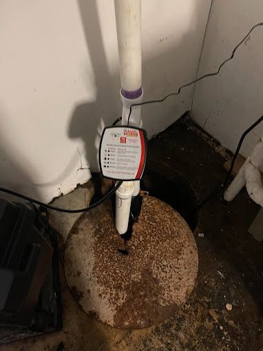 A sump pump with a white pipe and sensor box in a basement corner.