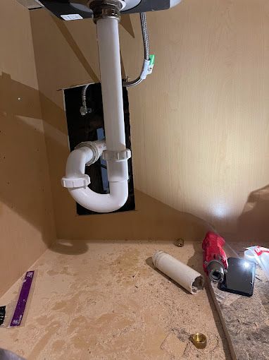 Under-sink plumbing with a white p-trap, pipes, and open cabinet, possibly under renovation.