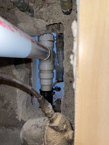 Plumbing repair: White and gray pipes, some inside a wall. A wrench and a white tube are in use.