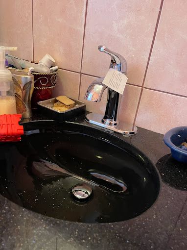 Black sink with chrome faucet and soap dispensers on a pink-tiled wall.