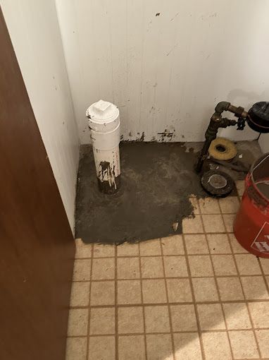 Concrete patch around a white plumbing pipe and old gas fixtures in a tiled corner.