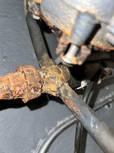 Rusty metal pipe fittings connected with tubing against a dark gray surface.