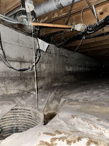 Crawl space with concrete walls, pipes, and a drain. Dark, damp environment with potential water damage.