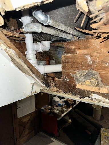 Plumbing pipes and electrical conduit exposed in a damaged wood-framed wall.