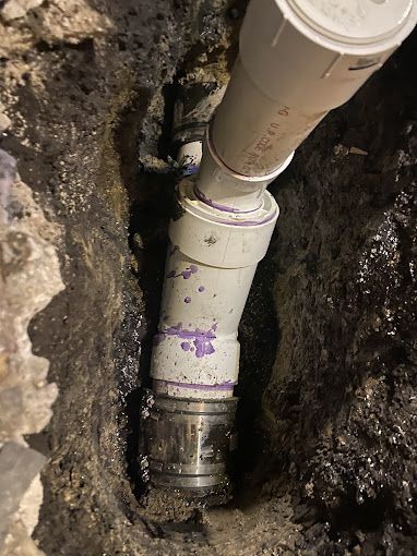 White PVC pipes connected in a trench, with a metal coupling. Purple markings on the pipes.